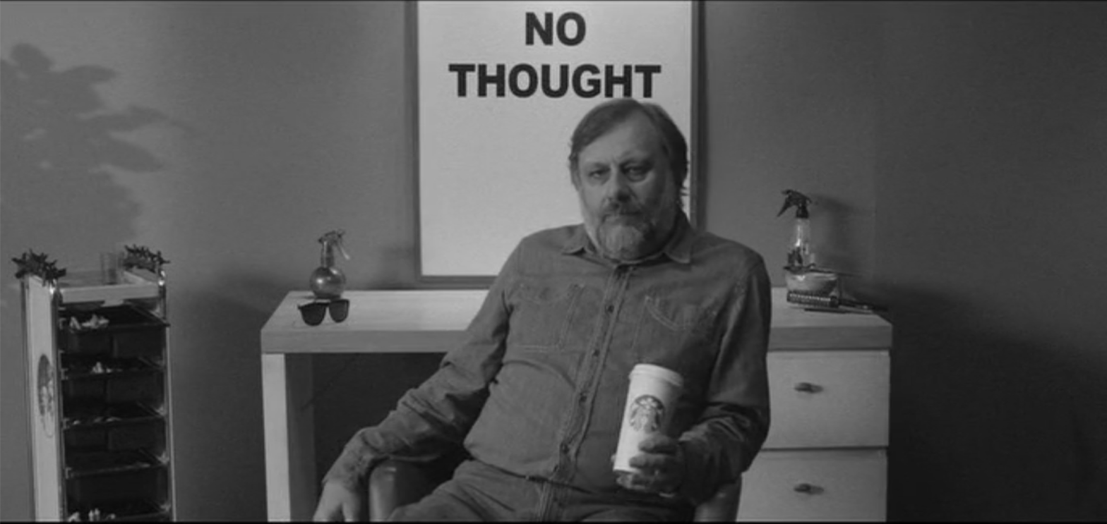 Screen capture from The Pervert's Guide to Ideology featuring Zizek and a cup of Starbucks Coffee sitting in front of a poster that says "No Thought"